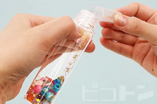 ワークショップの流れのカラフルビーズを選び、ラメと一緒にボトルに入れている画像