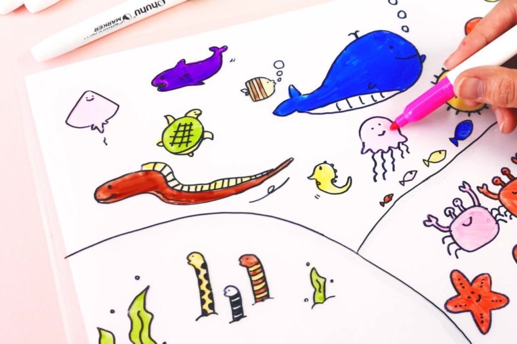 100円ショップのクリアファイルに描いた海の生き物に油性ペンで色を付ける様子