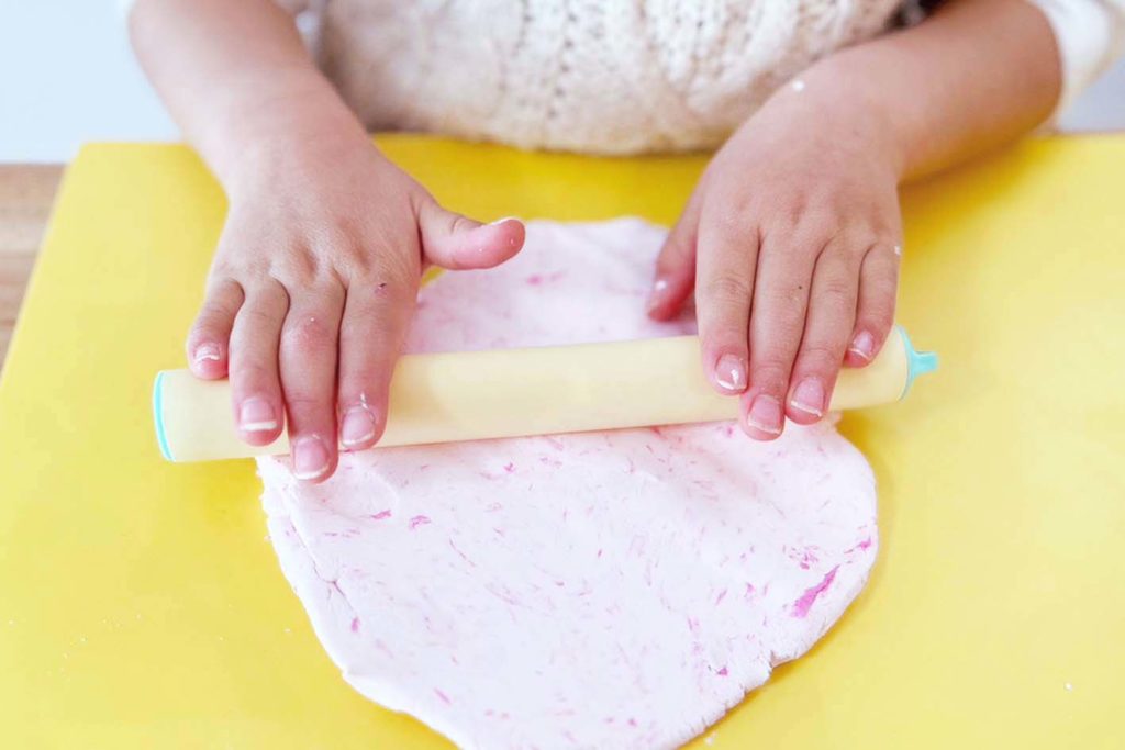 伸ばし棒で粘土で広げる子供。粘土がうすピンクになっている。