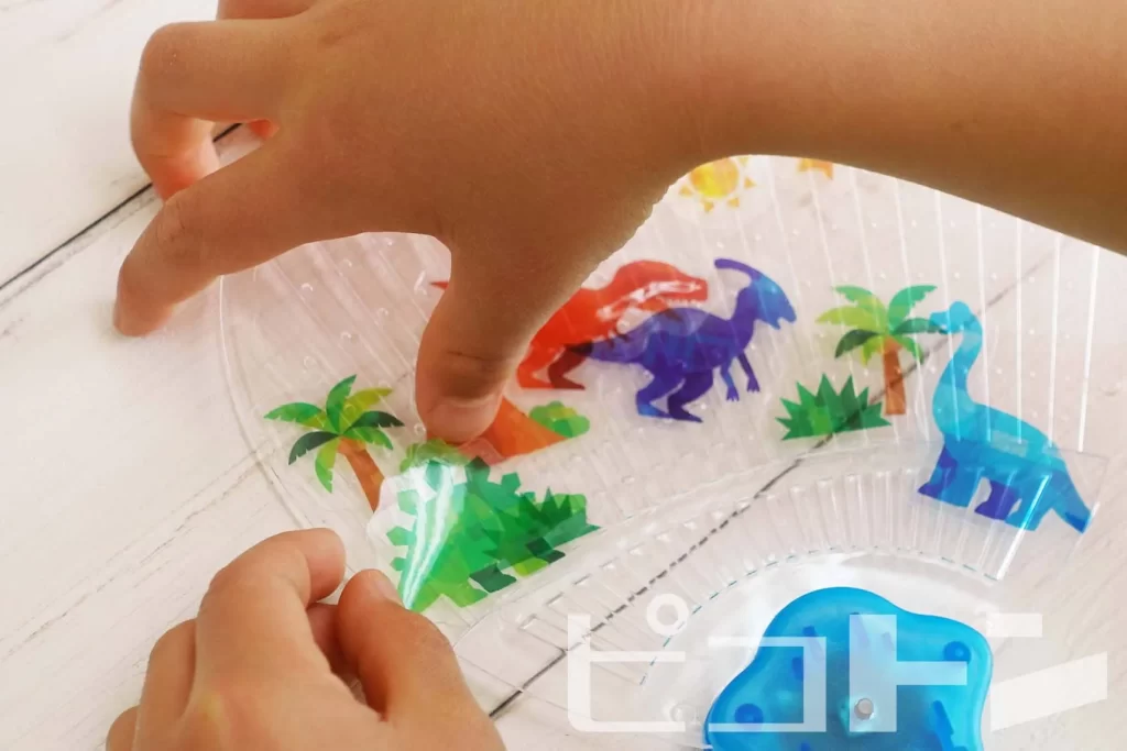 透明うちわに恐竜のシールを貼る子供の手元