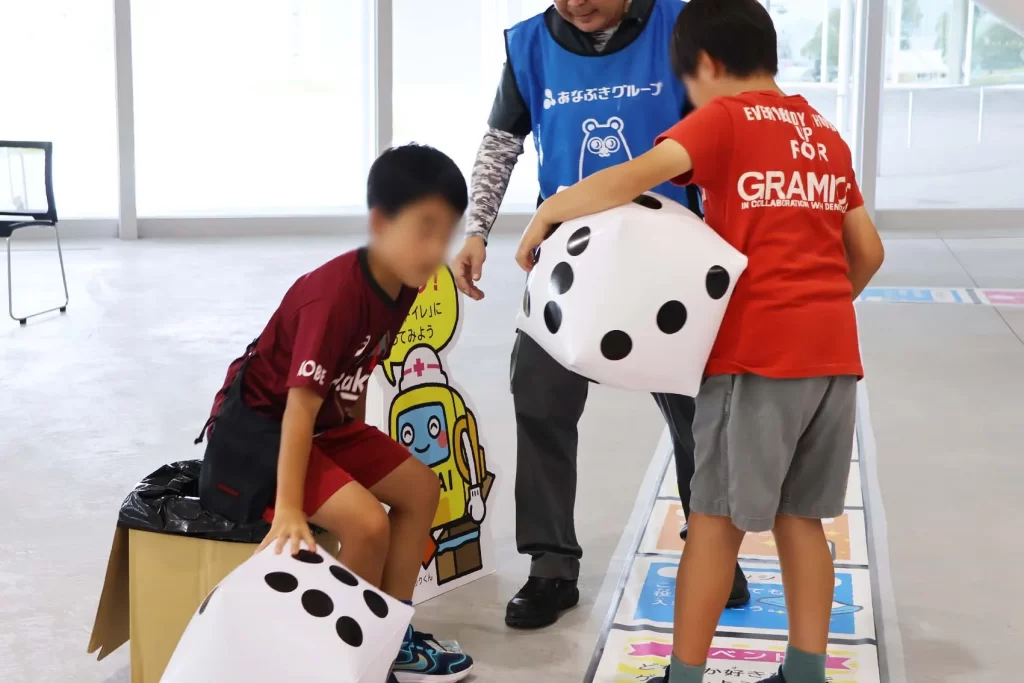 簡易トイレに座る男の子とサイコロを持つ男の子