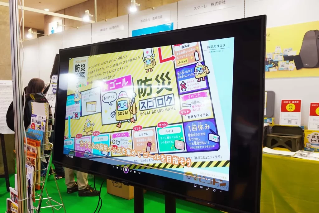 東京ビッグサイトにて開催された「第100回東京インターナショナルギフトショー 秋2025」の防災グッズ大賞2025のモニターに『防災スゴロク』が映る様子