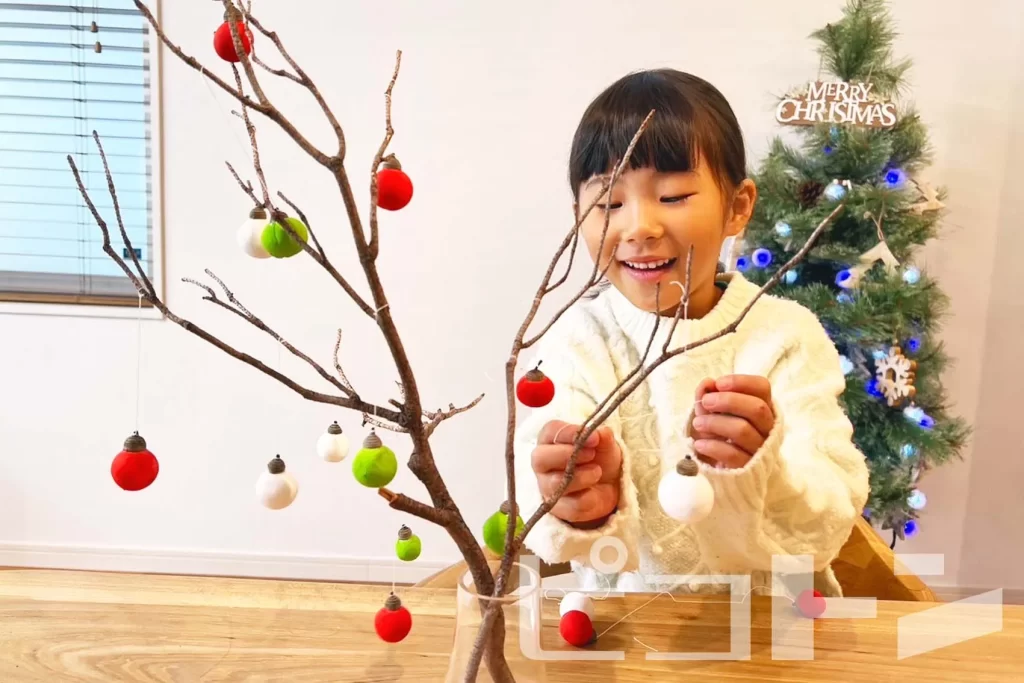 木の枝にクリスマスの飾りを取り付ける女の子
