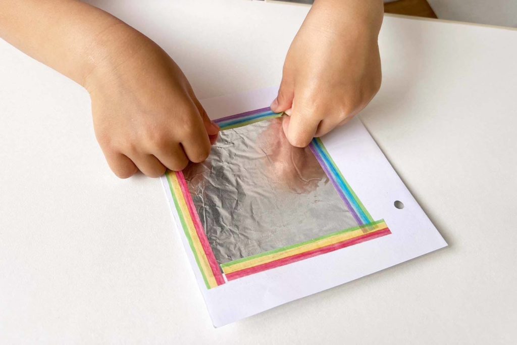 マスキングテープを使いアルミホイルを画用紙に貼る女の子の手元
