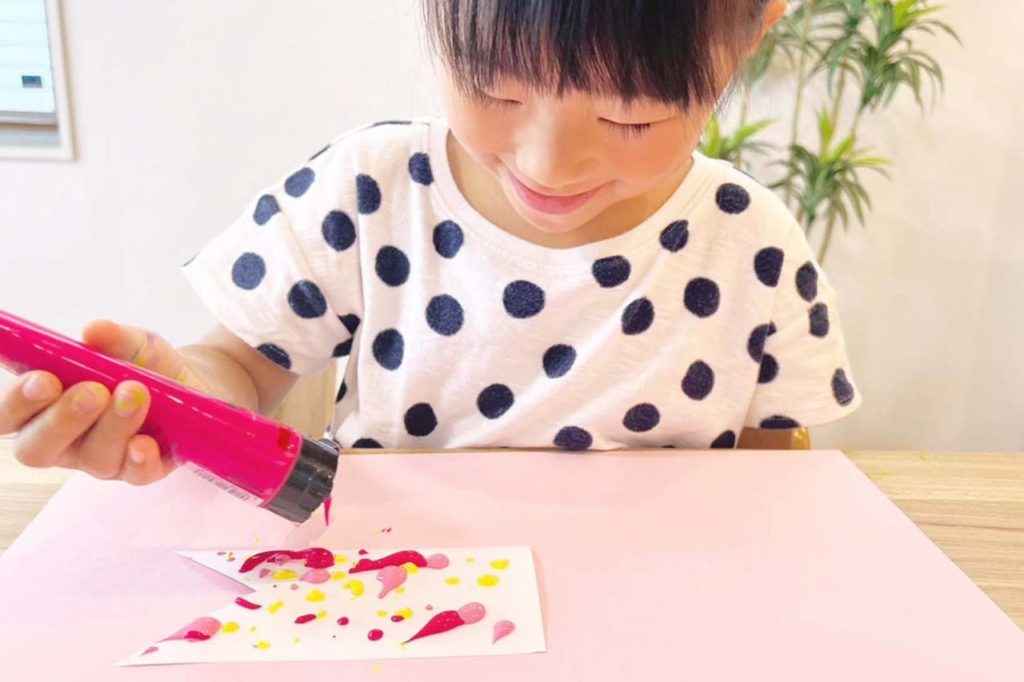 こいのぼりの形に切った画用紙にピンクの絵の具を出している女の子