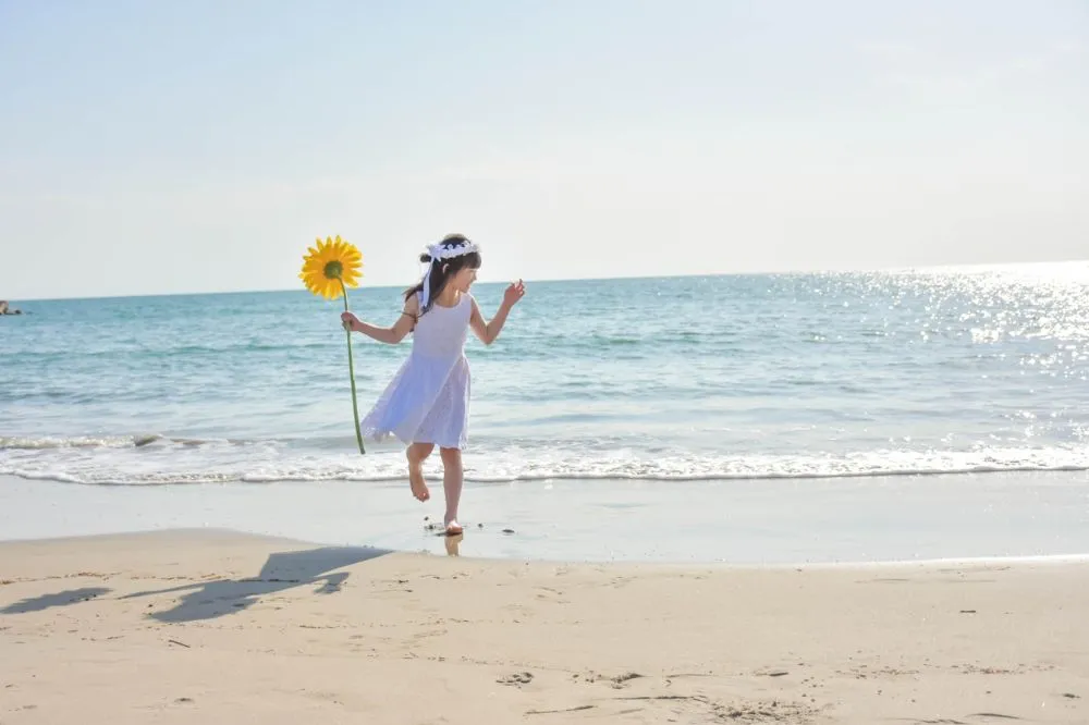 向日葵を持って海辺を走る女の子