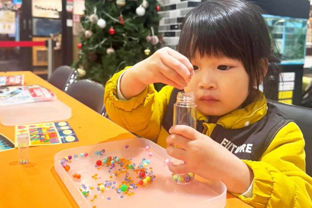 『光る!ウォータースティックライト クリスマスver.』のボトルにビーズを入れる子供