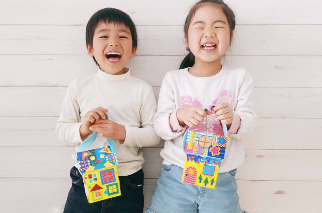 子供向け工作ワークショップ「Myおうちバッグ」の完成品をもって楽しそうな笑顔を見せる男の子と女の子