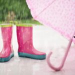 雨の中にピンクの長靴と傘が置いてある梅雨のイメージ