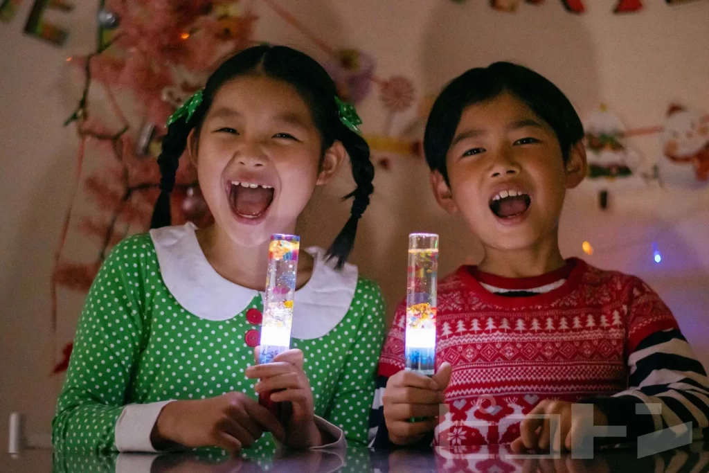 暗い場所で『光る！ウォータースティックライト クリスマスver.』を光らせる男の子と女の子