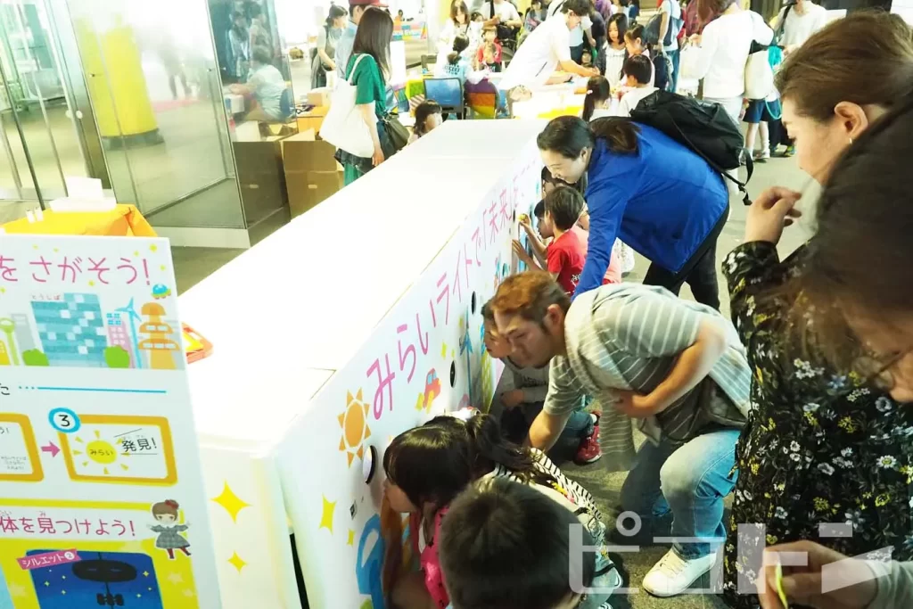 東芝未来科学館の5周年イベントの『光る! ウォーターみらいライト』の特製ボックスに並ぶ親子